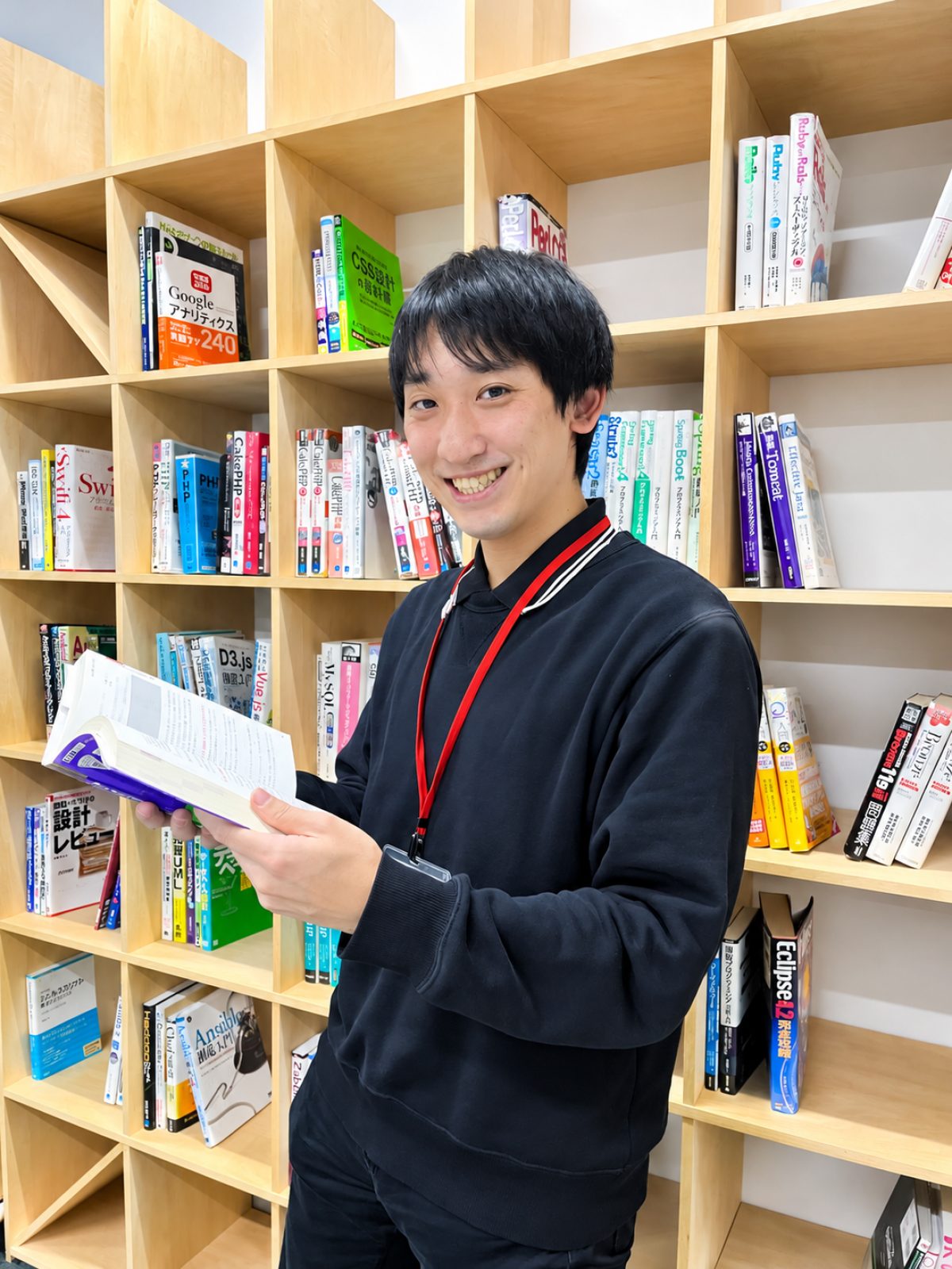技術書が並ぶ本棚の前で本を読む社員