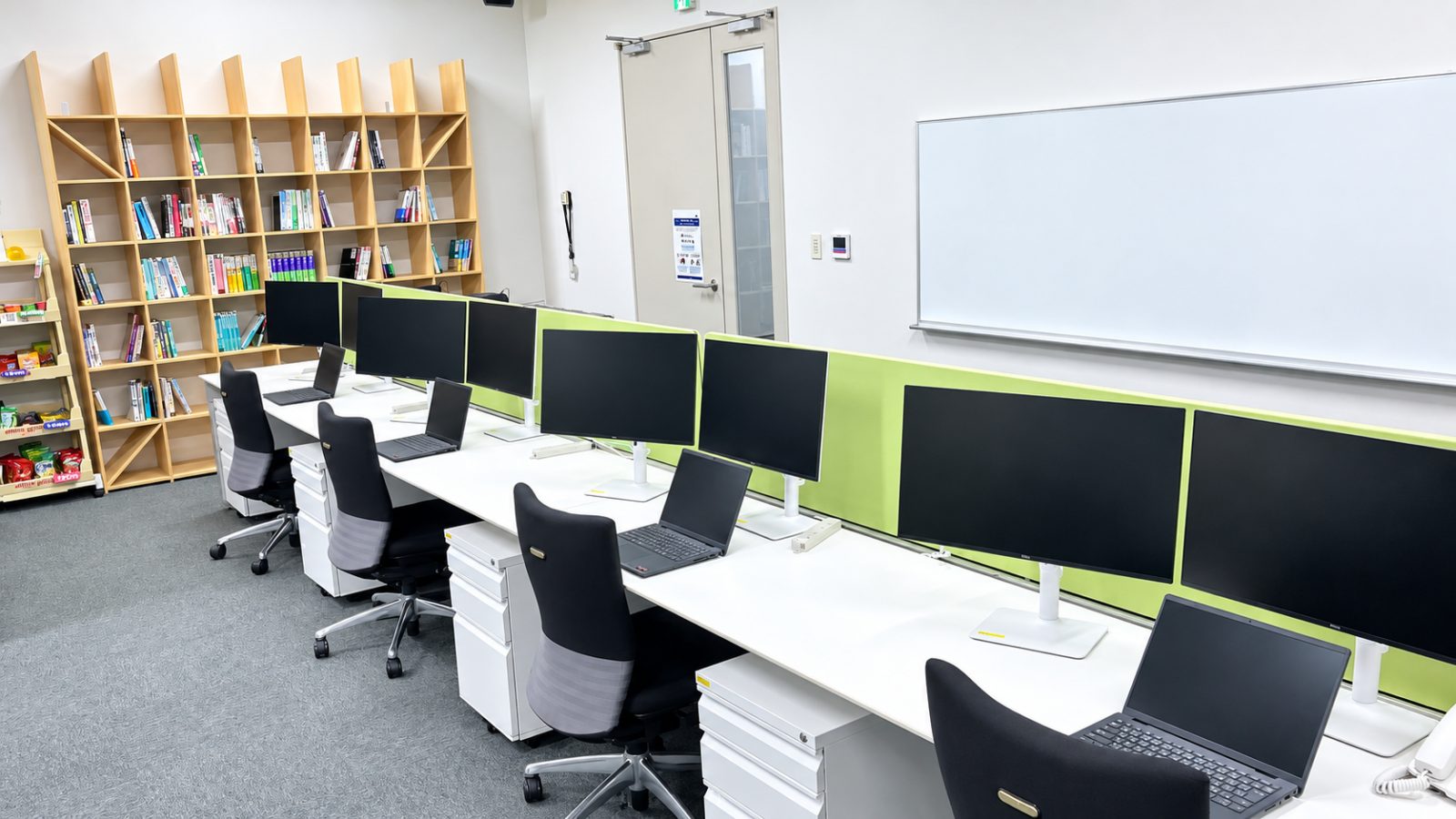 ノートパソコンと液晶モニタが並ぶ執務スペースと壁付けのホワイトボード